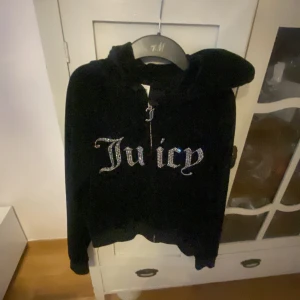 Svart zip hoodie från Juicy Couture äkta  - Snygg svart hoodie från Juicy Couture med glittrande text på framsidan. Perfekt för en avslappnad och stilren look. Den har en dragkedja och en mysig huva.