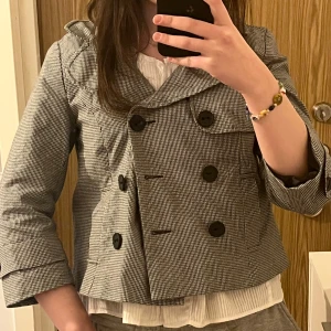 Grå rutig jacka  - Snygg svart vit rutig trenchcoat med dubbelknäppning och trekvartsärmar. Perfekt till vår! Passar s/xs då jag anser att den är lite liten i storleken. Mycket bra skick.
