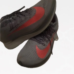 Grå och röda Nike löparskor - Snygga grå Nike löparskor med en iögonfallande röd swoosh. Skorna har snörning och en bekväm passform, perfekta för löpning och träning. Den grå färgen kombineras med en röd detalj för en sportig look.  Ny pris: 3000kr