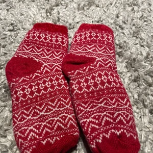 Röda mönstrade strumpor - Säljer ett par mysiga röda strumpor med vitt mönster. Ena sidan är helt röd och den andra har ett fint, traditionellt mönster. Perfekta för att hålla fötterna varma och stiliga. Inte använda