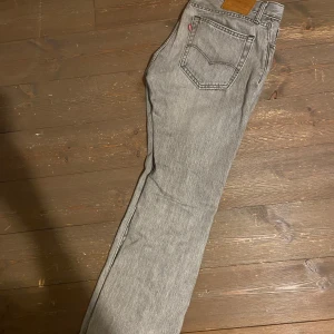 Grå jeansbyxor från Levis - Säljer ett par grå Levis jeans med klassisk femficksdesign och en snygg, sliten look. Byxorna har en rak passform och är tillverkade i slitstarkt denim. Perfekta för en avslappnad stil. Har även ett litet håll längst nere på jeansen 