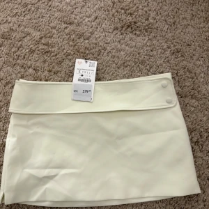 Ljusgul kjol från Zara - Snygg ljusgul kortkjol från Zara med en stilren design. Kjolen har en bred linning och knappar på sidan för en modern touch. Perfekt för att skapa en chic look.