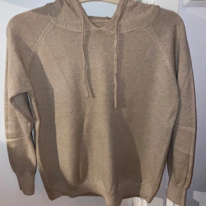 Merinoull hoodie - Säljer en stilren beige merinoull hoodie med långa ärmar och justerbar huva. Perfekt för kyliga dagar och enkel att matcha med olika outfits. 100 % meinoull
