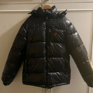 Svart shiny Ralph Lauren puffer down jacket - Svart glansig puffer dunjacka från Ralph Lauren med röd broderad logga på bröstet. Perfekt till den kyliga vintern som råder! Har ej kvitto eller andra äkthetsbevis, därav låga priset! Skriv gärna vid övriga frågor🙌🏻