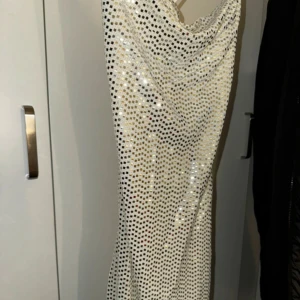 Vit glittrig klänning med smala axelband - Snygg vit klänning med glittriga paljetter och smala axelband. Perfekt för en festlig kväll med sin eleganta design och skimrande yta.