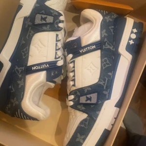 Blå och vita sneakers från Louis Vuitton - KOM MED BUD ! Snygga sneakers från Louis Vuitton i blått och vitt med det ikoniska monogrammönstret. Skorna har snörning och en robust sula med märkets logotyp. Perfekta för den stilmedvetna som vill ha något unikt. Helt nya passade inte mig tyvärr 