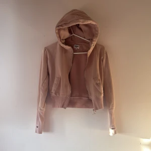 Beige hoodie med text - Säljer en beige hoodie med dragkedja och texten 'DEDICATION' på ryggen. Den är av kortare model som slutar strax över höfterna.