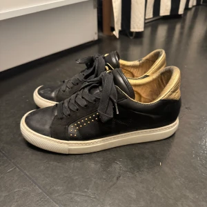 Zadig Voltaire sneakers  - Snygga svarta sneakers med gulddetaljer och snörning. Har bytt sula från den original sulan man fick med. Dem är dekorerade med små guldfärgade nitar på sidorna. Insidan är också i guld vilket ger en lyxig känsla.