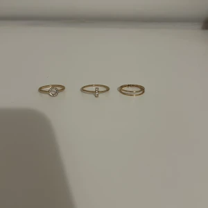 Fina guldiga ringar - Säljer tre fina guldiga ringar, en med en cirkel med ”diamant liknande stenar” och en med ett ”streck” med ”diamant liknande stenar” och en dubbelring i storlek S/M från Bershka🩷går att bara köpa en eller två ifall man inte vill ha alla tre, isåfall kan vi diskutera priset💕knappt använda och priset går att diskutera😇😇
