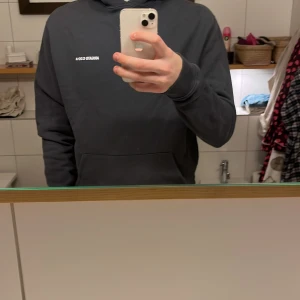 Mörkblå hoodie från Axel Arigato - Säljer en stilren mörkblå hoodie från Axel Arigato med vit text på bröstet. Tröjan har en klassisk design med känguruficka och långa ärmar. Perfekt för en avslappnad look.