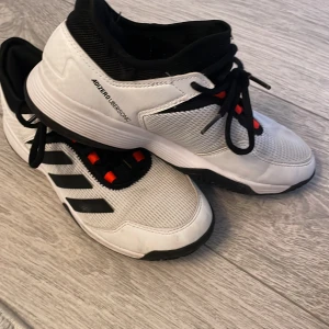 Adidas Adizero Ubersonic sneakers - Snygga Adidas Adizero Ubersonic sneakers i vitt med svarta och röda detaljer. Skorna har en sportig design med snörning och är perfekta för träning. De har en bekväm passform och slitstark sula.