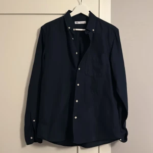 Mörkblå skjorta från Zara - Snygg mörkblå bomull/linne skjorta från Zara med klassisk design och vita knappar. Perfekt för en stilren look. En sprillans ny skjorta från Zara, aldrig använd! Skjortan var för liten för mig och tog inget kvitto så kunde inte lämna tillbaka skjortan. Nypris 600kr, mitt pris 400kr