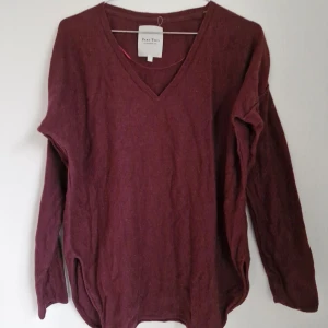 Vinröd tröja från Part Two - Säljer en vinröd tröja från Part Two i storlek M. Tröjan är tillverkad av 90% bomull och 10% kashmir, vilket gör den mjuk och bekväm. Den har en v-ringad hals och långa ärmar, perfekt för kyligare dagar. Finns ett litet hål på baksidan vid halsen, annars är den i fint skick!