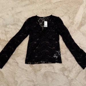 Spetstopp - Säljer en svart spetstopp från Gina Tricot i strl M. Helt ny med alla lappar kvar. Toppen har ett blommönster och långa ärmar. 