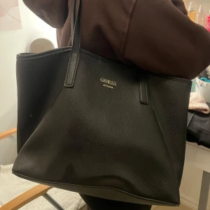 Svart väska från Guess - Snygg svart väska från Guess med leopardmönstrat foder. Väskan har två långa handtag och är perfekt för att bära med sig allt man behöver. Den stilrena designen gör den lätt att matcha med olika outfits. Nypris ca 1200kr💗💗