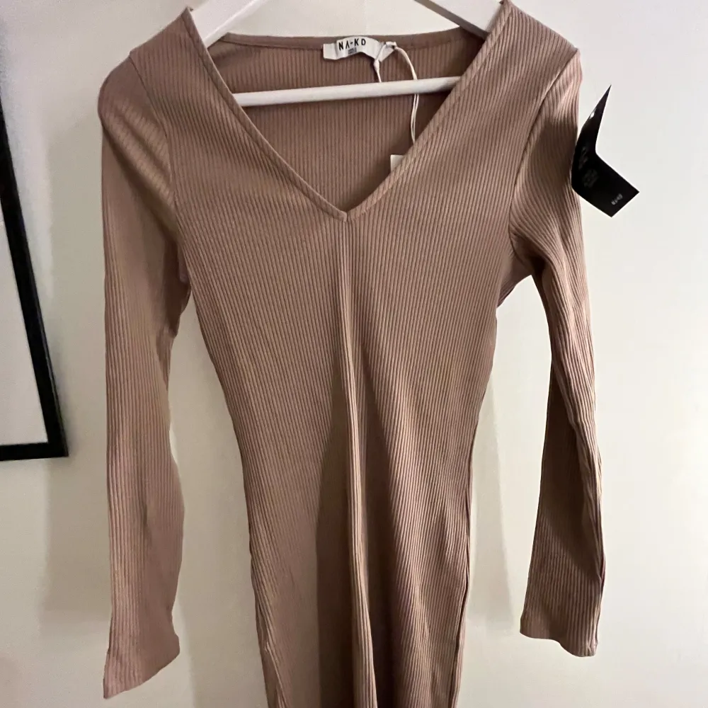Säljer en stilren beige ribbad klänning från NA-KD. Klänningen har en v-ringad design och långa ärmar, perfekt för en chic look. Den är figurnära, storlek m men passar även s och xs då den är tajt med stretchiga material. Aldrig använd med prislappen kvar😊. Mekot.