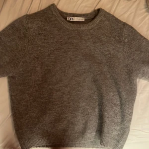 Grå stickad tröja från Zara - Säljer en mysig grå stickad tröja från Zara. Tröjan har en rund halsringning och ribbade muddar vid ärmslut och nederkant. Perfekt för kyliga dagar!
