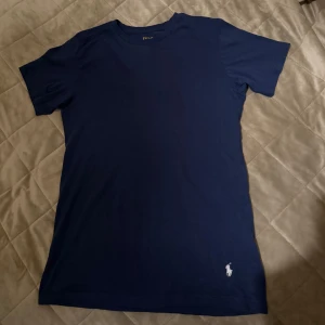 Ralph Lauren t-shirt - Säljer en stilren mörkblå t-shirt från Ralph Lauren med klassisk passform. T-shirten har en liten vit logga på framsidan och är tillverkad i mjuk bomull. Perfekt för en avslappnad look.