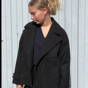 Svart kappa - Snygg svart kappa med dubbelknäppning och breda slag. Jackan har långa ärmar och en stilren design som passar perfekt för kyligare dagar. Den är från design by si och kostar 600kr som ny
