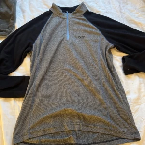 Grå och svart tröja från Kayoba - Säljer en grå och svart tröja från Kayoba med dragkedja vid halsen. Perfekt för utomhusaktiviteter. Tröjan har långa ärmar och är tillverkad i ett bekvämt material.