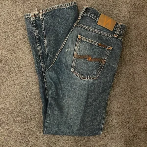 Blåa nudie jeans - Snygga blå jeans från Nudie Jeans med klassisk femficksdesign och orange sömmar. Dem är i använt skick och har en liten slitning på baksidan och en slitning längst ner på det högra benet. Skick 7/10 storlek W30 L32 pris kan disskuteras, medela mig vid frågor