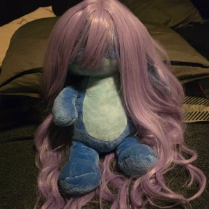 Lång lila peruk - Säljer en lång, vågig peruk i en vacker lila nyans. Perfekt för cosplay eller att förändra din look. Peruken har en naturlig glans och är lätt att styla.
