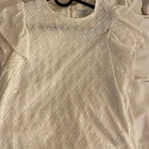 Vit blus från Holly & White - Säljer en elegant vit blus från Holly & White med ett vackert mönster och volangdetaljer på ärmarna. Perfekt för en stilren look.