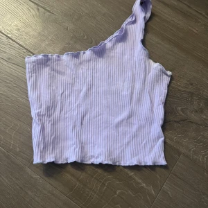 Ljuslila ribbad oneshoulder topp - Säljer en snygg ljuslila oneshoulder topp med ribbad struktur. Perfekt för en trendig look. Toppen är i en mjuk och bekväm design.