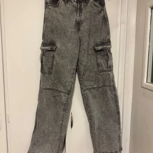 Grå cargopants - Snygga grå cargopants med flera praktiska fickor på sidorna. Byxorna har en loose passform och är perfekta för en avslappnad stil. De är tillverkade i ett slitstarkt material som ger en cool look.