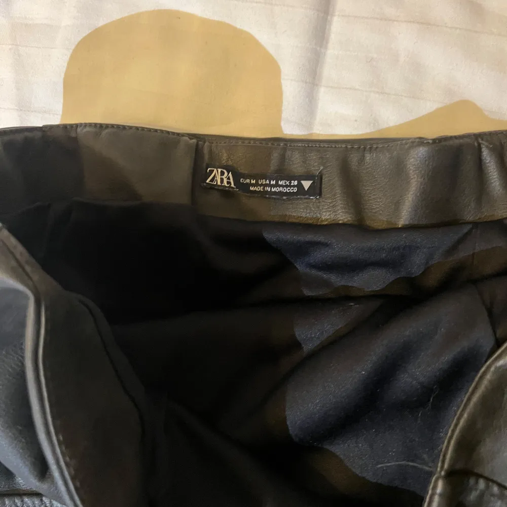 Snygg svart axelbandslös jumpsuit från Zara i skinnimitation. Perfekt för en cool och stilren look. . Mekot.