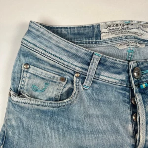 Ljusblå jeans från Jacob Cohen - Snygga ljusblå jeans från Jacob Cohen med en klassisk femficksdesign och broderad logga på myntfickan. Jeansen har en knappgylf och är tillverkade i ett mjukt denimtyg som ger en bekväm passform. Perfekta för en avslappnad stil. Storlek: W29