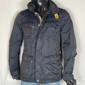 Parajumpers Field Jacket - Svart safarijacka från Parajumpers med flera fickor och en dragkedja framtill. Jackan har en hög krage och en gul detalj vid halsen. Skick: 8/10. Retail: ~6000kr. 