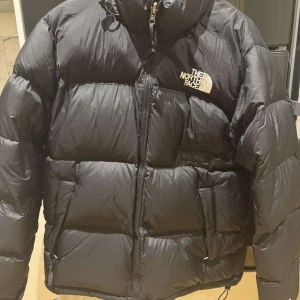 Svart dunjacka från The North Face - Säljer en svart dunjacka från The North Face. Jackan har en dragkedja framtill och är långärmad med en hög krage för extra värme. Perfekt för kalla dagar. Pris går att diskuteras!!!