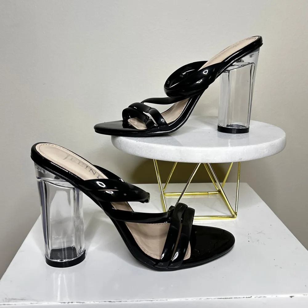 Svarta klackskor från Jeeni med en modern transparent klack. Skorna har flera smala remmar över foten som ger en elegant look. . Kengät.