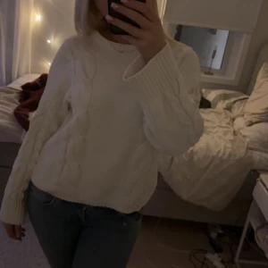 Vit stickad tröja - Mysig vit stickad tröja med kabelstickat mönster. Perfekt för kyliga dagar med sin varma och bekväma design. Tröjan har långa ärmar och en klassisk rund halsringning.