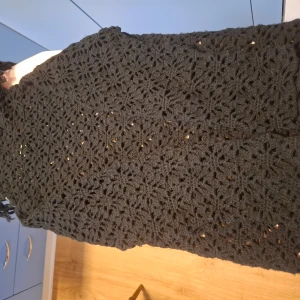 Svart stickad polotröja från Gudrun Sjödén - Säljer en svart stickad polotröja från Indiska med ett vackert hålmönster. Perfekt för att hålla sig varm och stilren under kyligare dagar. Polotröjan har en elegant design med fransar på halskragen o längst ner på kanten av tröjan 