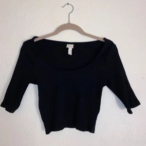 Svart ribbad topp från H&M - Snygg svart ribbad topp från H&M med trekvartsärm och en djup rund halsringning. Perfekt för en stilren look. Passar bra till både jeans och kjol.