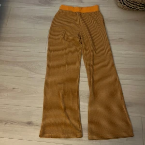 Randiga byxor i gult och brunt - Snygga randiga byxor i gult och brunt med en bekväm passform. Byxorna har en elastisk midja och vida ben, vilket ger en avslappnad stil. Perfekta för en trendig look.