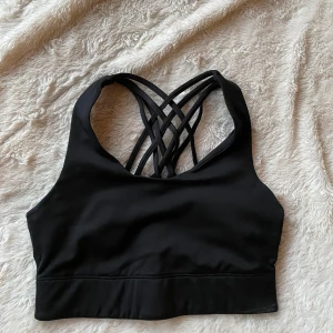 Svart sport-bh med korsade band - Snygg svart sport-bh med korsade band i ryggen. Perfekt för träning med sin bekväma passform och stilrena design.