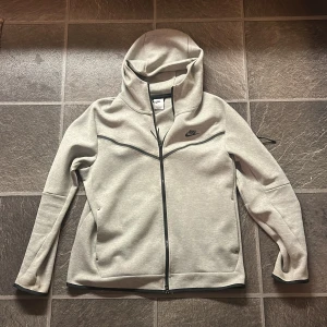 Grå hoodie från Nike - Säljer en stilren grå hoodie från Nike med dragkedja och svart logga på bröstet. Den är knappt använd och köpt i butik! Den passar även M men bäst som L.