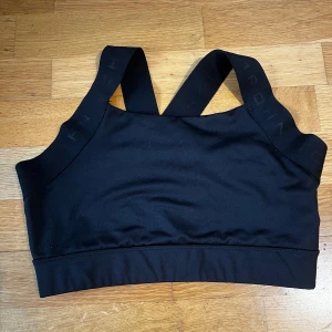 Svart sporttopp från Röhnisch - Snygg svart sporttopp från Röhnisch med breda axelband och elastisk kant. Perfekt för träning med sin bekväma passform och stilrena design.