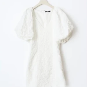 Vit klänning med puffärmar - Säljer en elegant vit klänning med puffiga kortärmar och v-ringning. Klänningen har en texturerad yta som ger en unik look. Perfekt för sommarens alla tillfällen! Anledningen till att jag säljer den är för att jag hittade en annan klänning till min student. Denna är super fin och figuraydd.💞(slutsåld, med prislapp och påse) 