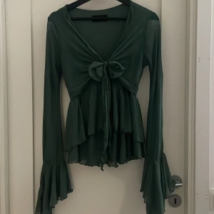 Grön blus från Cider - Snygg grön blus från Cider med långa utsvängda ärmar, mycket volanger och en fin knytning där fram. Den är figursydd så den sitter jättefint på + materialet är superskönt. Använt fåtalgånger men är i fint skick.
