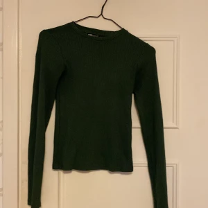 Mörkgrön ribbad tröja från FB Sister - Säljer en stilren mörkgrön ribbad tröja från FB Sister. Tröjan har en klassisk design med långa ärmar och rund halsringning. Perfekt för en avslappnad och trendig look. Passar bra till både jeans och kjol.