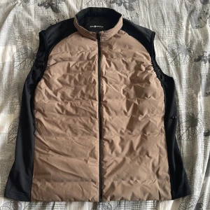 Beige och svart väst från SAIL RACING - Snygg beige och svart väst från SAIL RACING med dragkedja framtill. Perfekt för lager-på-lager under kyligare dagar. Västen har en stilren design och är lätt att matcha med olika outfits.