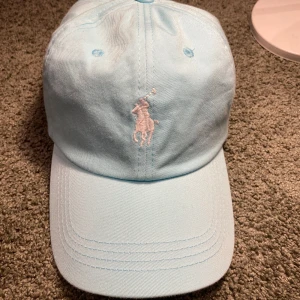 Ljusblå keps från Polo - Snygg ljusblå keps från ralphlauren. Aldrig använd och inga skador eller fläckar på kepsen. Justerbar rem baktill. Tillverkad i 100% bomull för en bekväm passform. En Nice keps till at matcha outfits med! Skriv vid fler frågor el funderingar!