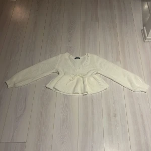 Vit stickad tröja från Shein - Säljer en vit stickad tröja från Shein med v-ringning och knytband i midjan. Tröjan har långa ärmar och en volangdetalj vid nederkanten. Perfekt för en stilren och mysig look ✅