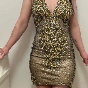 Glittrig klänning med paljetter - Snygg och glittrig klänning med djup v-ringning och paljetter över hela ytan. Klänningen har en smickrande passform och är perfekt för en festlig kväll. Den är axelbandslös och har en elegant design som verkligen sticker ut.