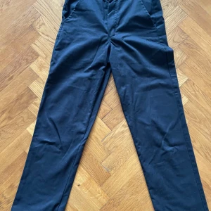 Svarta byxor från Dickies - Snygga svarta byxor från Dickies med en klassisk design. De har en dragkedja och knapp framtill samt en bakficka med knapp. Lite slitna i sömmen i bak men inget som syns med dem på!