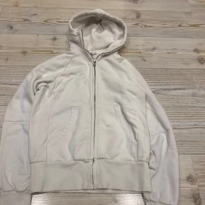 Vit hoodie från Vailent - Säljer en vit hoodie från Vailent med dragkedja och huva. Tröjan har ribbade muddar och fickor framtill. Perfekt för en avslappnad stil.